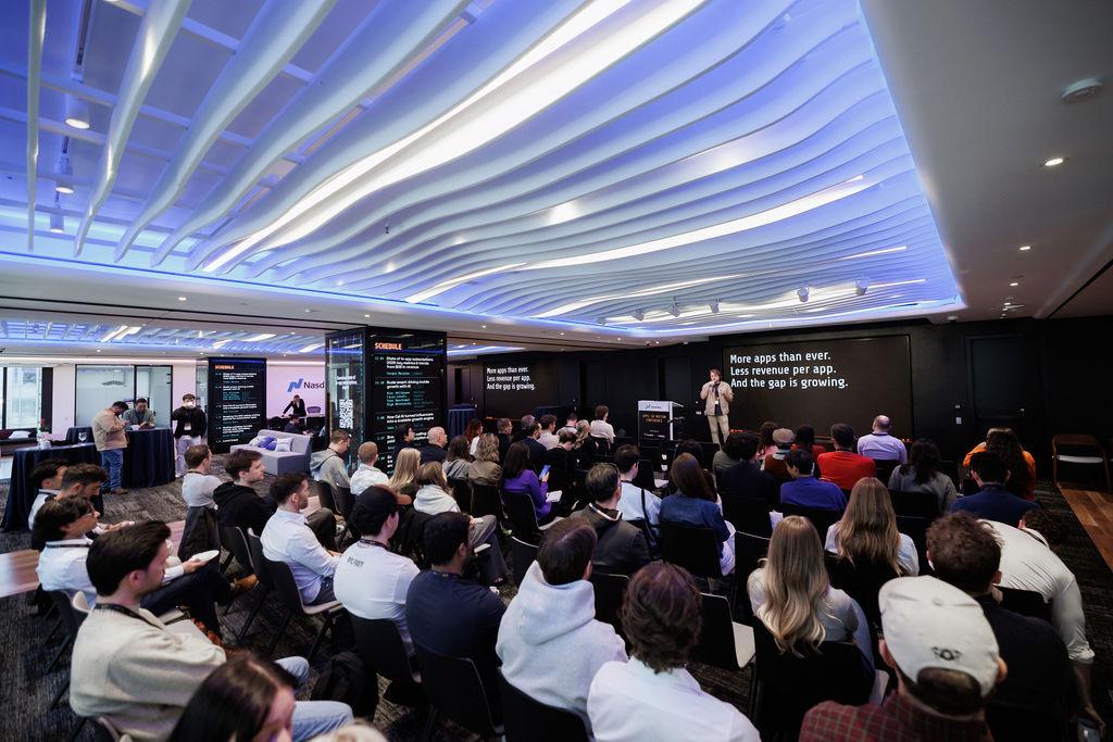 A full audience at the AIM Conference watching a panel beneath the venue's illuminated wave ceiling